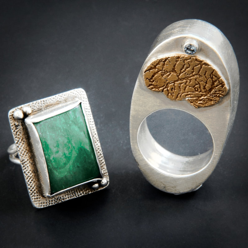Two silver handmade rings. One has a rectangular aquamarine stone. The other has a high profile with a gold brain and a blue stone on top.
